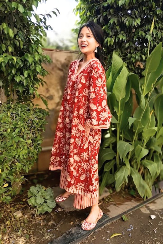 Image of a woman wearing a red floral Bagru print cotton kurta set with striped pants and juttis, standing in natural light