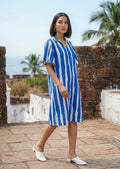 Woman wearing a blue and white striped dress standing on a stone path with a scenic background.