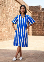 Woman wearing a blue and white striped dress standing in front of a brick wall.