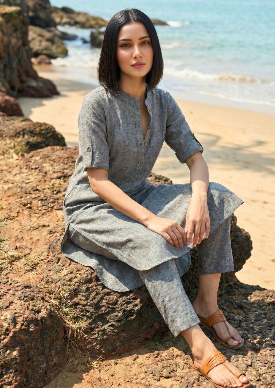 Woman sitting on a rock by the beach wearing a gray outfit.