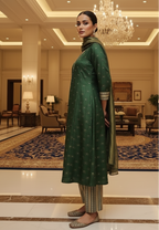 Woman in a green  silk traditional outfit standing in an elegant indoor setting with chandeliers and furniture.