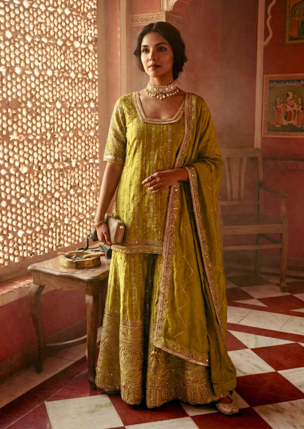 Woman in a traditional green outfit standing in a decorated room with pink walls and a patterned floor.
