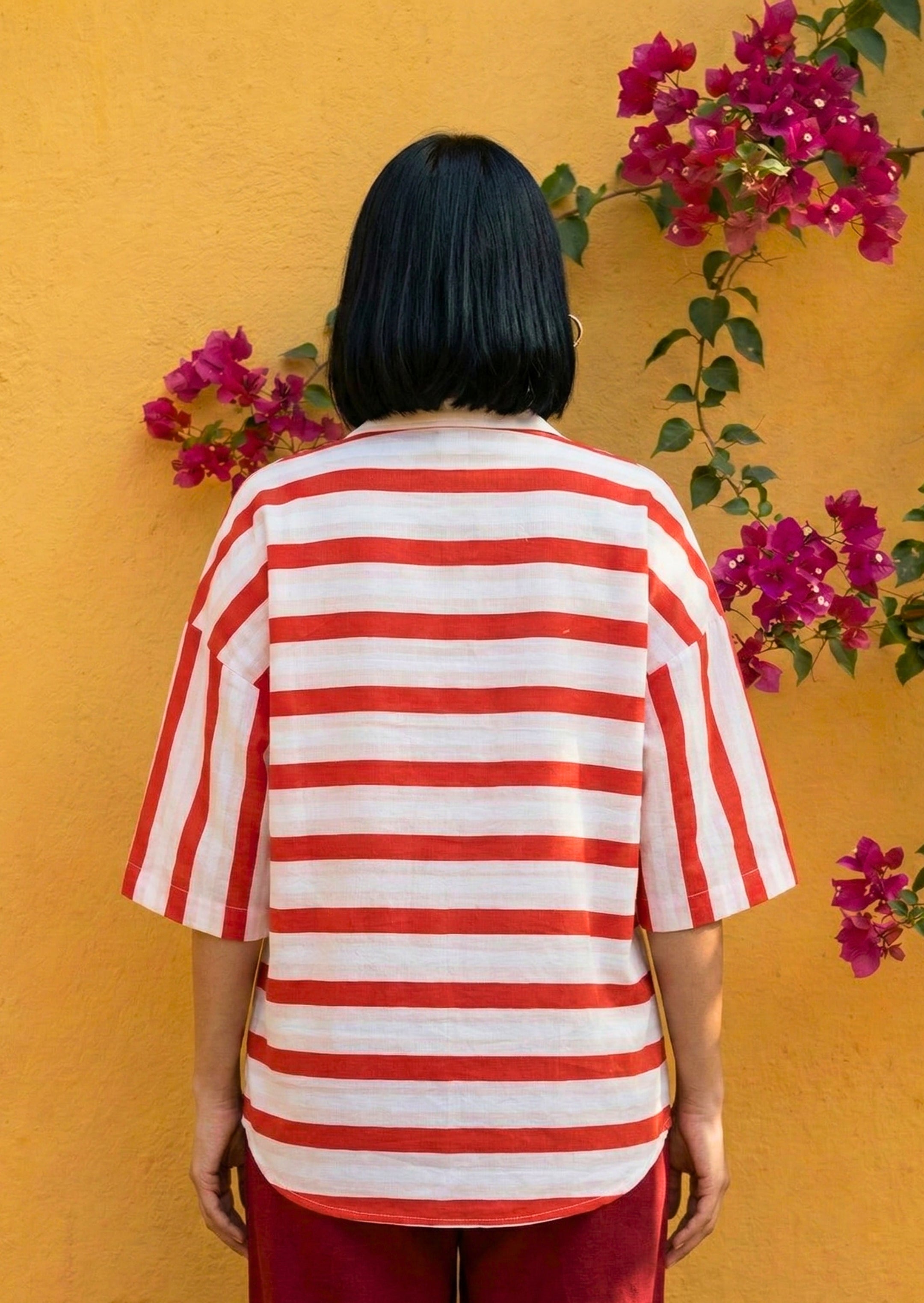 Person wearing a red and white striped shirt against a yellow wall with pink flowers.