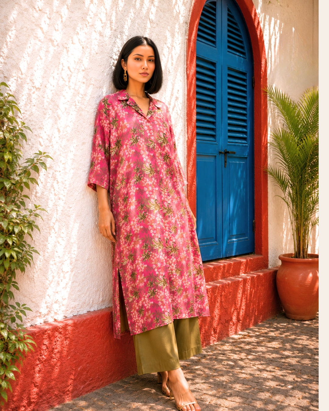 Woman in a pink floral dress standing in front of a blue door and white wall.