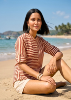 Woman sitting on a beach wearing a striped shirt and shorts with a scenic background.