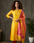 Woman wearing a yellow kurta with red pants and a pink dupatta against a gray background
