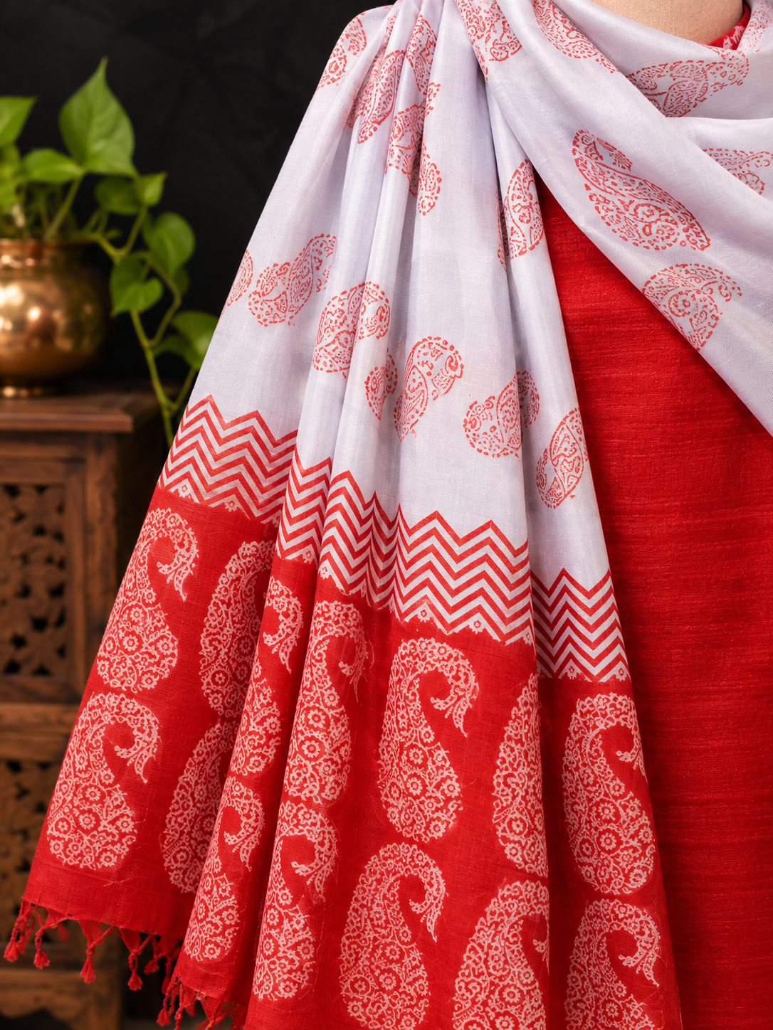 A close-up of a draped white and red silk dupatta with red paisley and chevron patterns, worn over a red garment.
