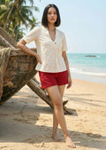 Woman wearing Bbaawri Kora Dobby Cotton Top in natural ivory with red shorts on a beach.