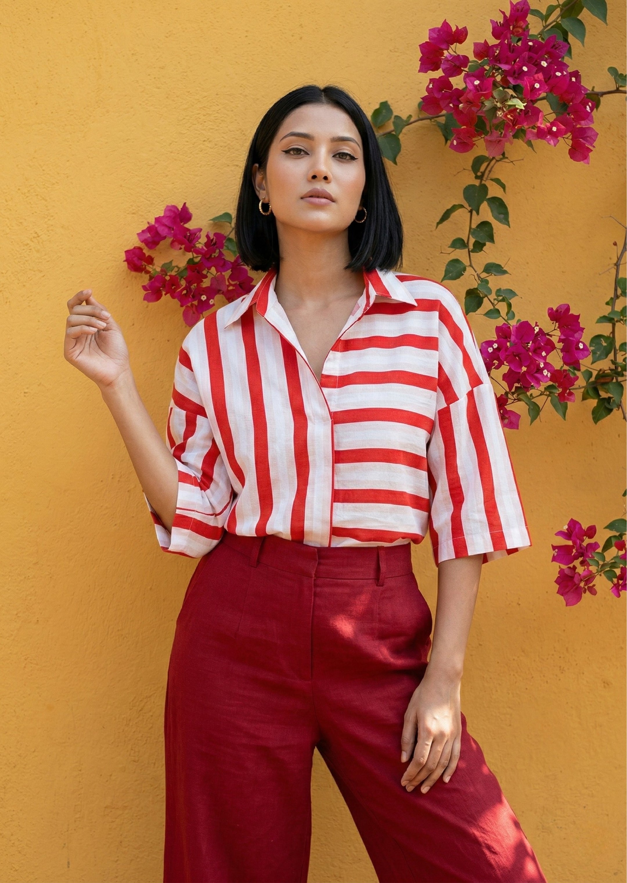 Woman wearing a red and white striped shirt and red pants against a yellow wall with pink flowers.