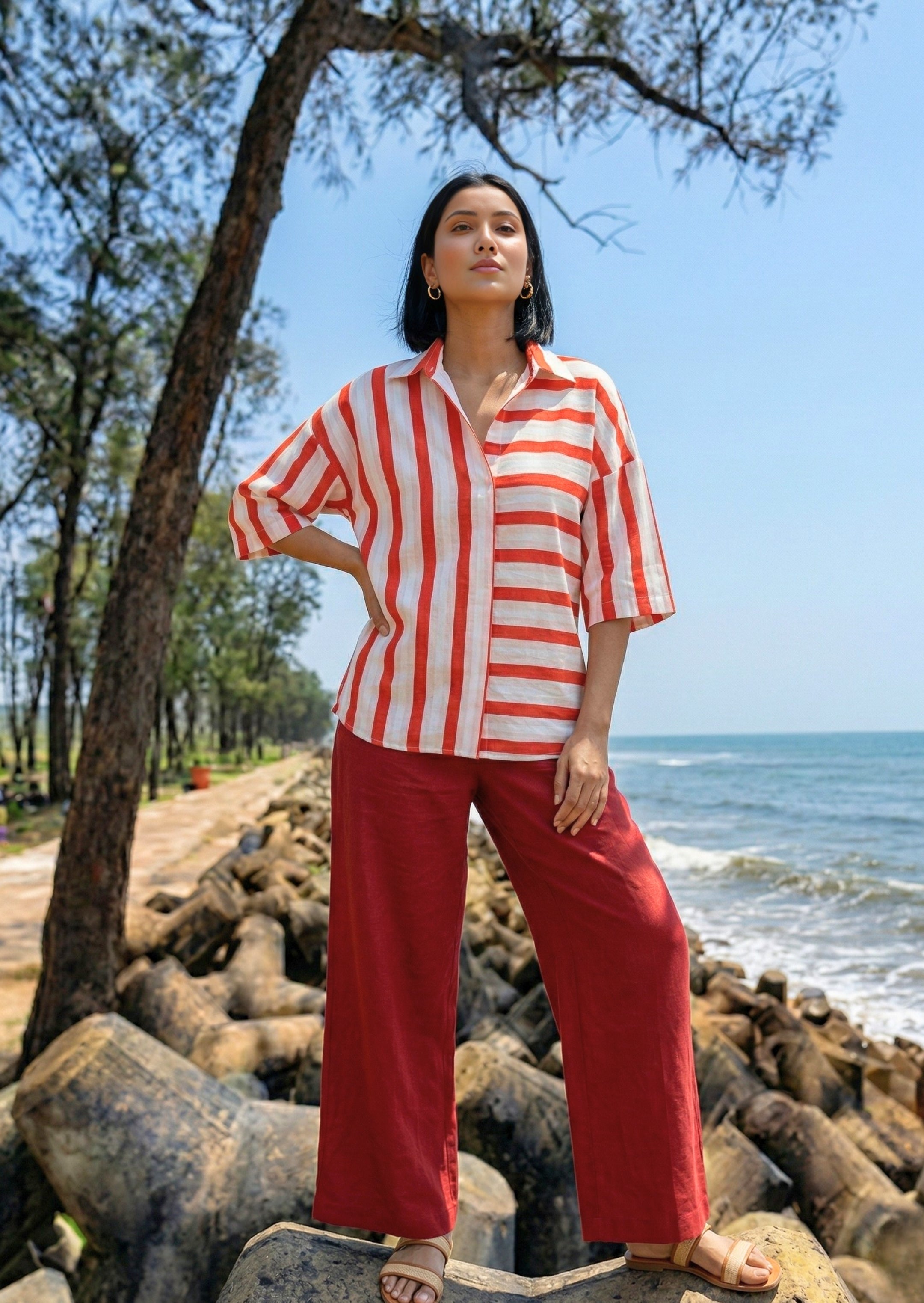 Woman in a red and white striped shirt and red pants standing on rocks by the ocean.
