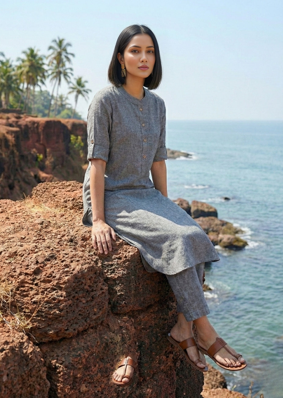 Woman in a gray outfit sitting on a rocky cliff overlooking the ocean.